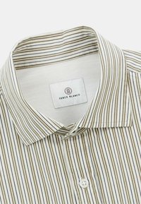 Chemise à col avec des rayures verticales beige, blanche et noire, montrant le premier bouton et l'étiquette intérieure.