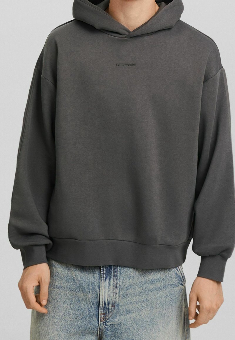 Sudadera con capucha de color gris oscuro y corte relajado, cuenta con un bolsillo tipo canguro, puños acanalados y un sutil logo grabado en el pecho.