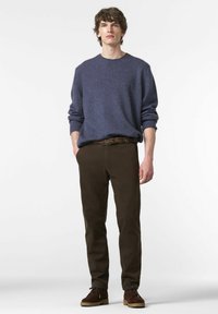 Donkerbruine chino's gecombineerd met een gestructureerde marineblauwe trui, met een ronde hals en opgerolde mouwen. Bruine suède schoenen maken de look af.