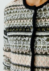 Gebreide cardigan met een ingewikkeld patroon van groene, zwarte, roze en witte garens, versierd met pailletten en een ronde sluiting.