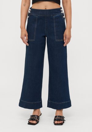 Bredde ben jeans i mørkeblå med høy midje, med store frontlommer og dekorative knappeakenter på sidene.