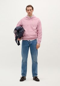 Lichtroze hoodiesweatshirt, blauwe jeans, zwarte schoenen en een donkere tas. Beschikt over witte trekkoorden, een kangoeroezak en een casual pasvorm.