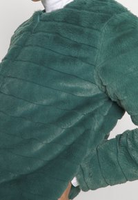 Maglione in pelliccia sintetica color teal con design testurizzato e sovrapposto e maniche lunghe. Presenta un collo rotondo e una leggera lucentezza sul tessuto.