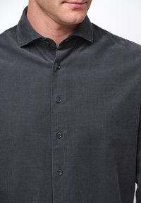 Camicia in corduroy grigio scuro con colletto, caratterizzata da una chiusura frontale con bottoni e sei bottoni. La texture è morbida e presenta righe verticali.