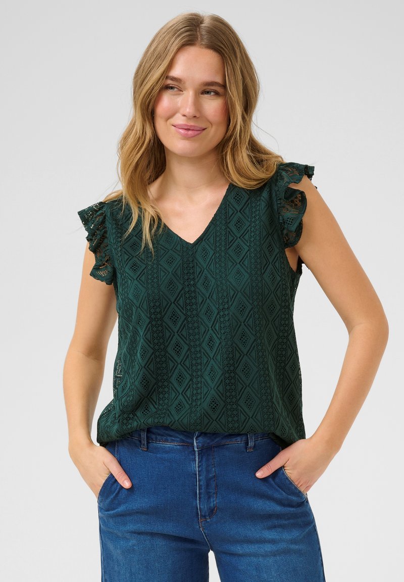 Haut sans manches vert à motifs avec un décolleté en V et des accents en dentelle froncée aux épaules, associé à un pantalon en denim bleu.
