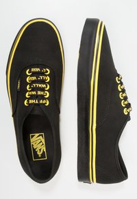 Mustia kanva kenkät, joissa on keltaisia yksityiskohtia, kuusi reikää ja paksut mustat kumipohjat, joissa on klassinen nauhakiinnitys.