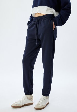 Marineblauwe sweatpants met elastische boorden en een drawstring taille, voorzien van zijzakken en een gladde textuur. Gecombineerd met lichte sneakers.