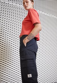 Rode cropped t-shirt met korte mouwen, gecombineerd met navy cargo pants met twee voorzakken en een Jordan-logo patch. Textuur achtergrond.
