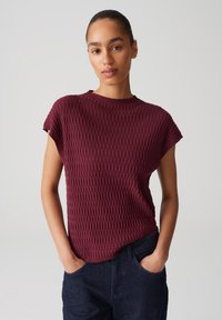 Maroon textured short-sleeve top with a round neckline, featuring a ribbed pattern. Paired with dark denim pants.