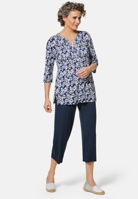 Blumen-Tunika in Marineblau mit weißen Blumen, Dreiviertelärmel, kombiniert mit marineblauen, cropped Hosen. Legere Espadrilles runden das Outfit ab.