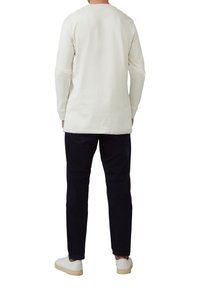 Cremfarbener Langarmshirt mit rundem Ausschnitt, kombiniert mit dunklen Hosen und weißen Sneakers, von hinten gezeigt.