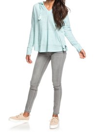 Himmelblauer, langärmeliger, kapuzenpulli mit lockerer Passform und seitlichen Schlitzen, kombiniert mit grauen Skinny-Jeans und hellbraunen Sneakers.