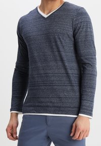 Marinblå långärmad V-ringad skjorta med ett texturerat randmönster och vit krage, tillverkad av ett mjukt, elastiskt tyg.