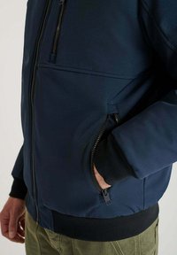 Giacca bomber blu navy con una texture liscia, tasche con zip e polsini a costine, caratterizzata da un design strutturato e dettagli con zip laterali.