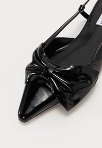 Black patent leather slingback shoe with pointed toe, featuring a bow accent on the vamp and thin adjustable strap. Smooth, shiny texture.