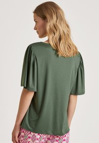 Groene top met korte mouwen en volants, gladde textuur, ronde halslijn en een ontspannen pasvorm, gecombineerd met gestreepte roze broek.