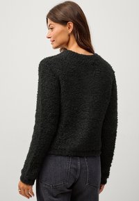 Schwarzer strukturierter Pullover mit Rundhalsausschnitt und langen Ärmeln, mit einem flauschigen Finish. Trägt eine hochgeschnittene dunkle Jeans.