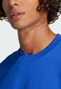 Maglietta di cotone blu con collo rotondo e maniche corte. Texture liscia, senza motivi o logo visibili. Vista ravvicinata dell'area del colletto.