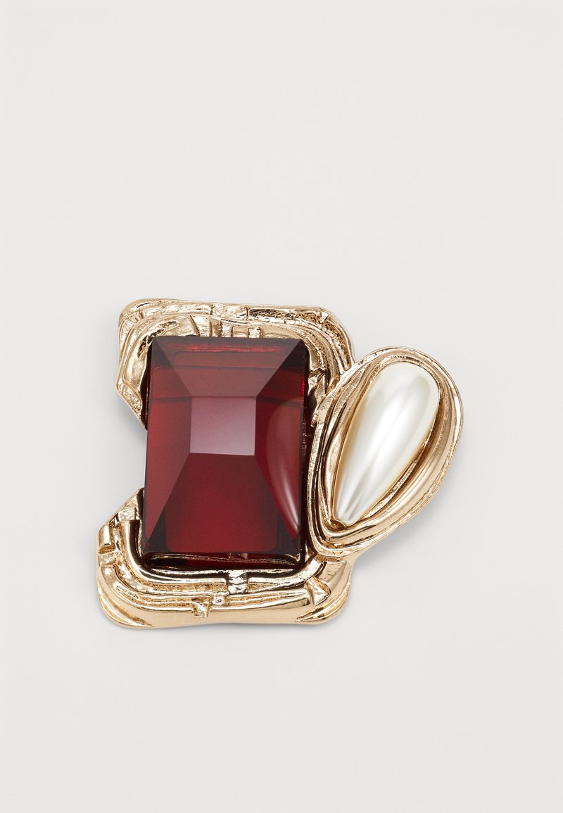 Hexagonal brooch featuring a large rectangular deep red gemstone and a pearlescent white accent, set in textured gold-tone metal.