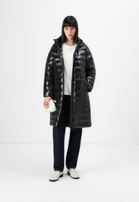 Piumino nero e lucido con cuciture orizzontali, colletto alto e zip frontale. Abbinato a un top bianco e jeans scuri.