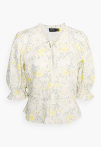 Vit blus med gult blommönster och gröna blad. Har en volangkrage, knytning och puffärmar med volangdetaljer.