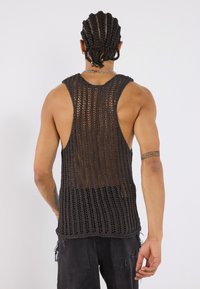 Schwarzes, gestricktes Tanktop mit offenem Häkelmuster, breiten Armöffnungen und lockerer Passform, das eine strukturierte Oberfläche und einen rohen Saum aufweist.