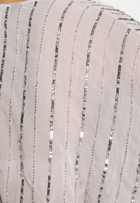 Tissu avec des rayures verticales de sequins argentés uniformément espacées sur un fond beige clair ou crème.