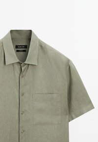 Camicia a maniche corte con bottoni in lino di un verde oliva chiaro. Presenta una tasca sul petto, colletto classico e bottoni abbinati.
