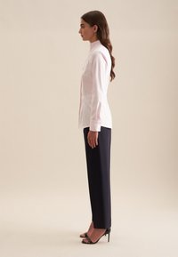 Camicia bianca a maniche lunghe con colletto alto, abbottonatura e vestibilità slim. Abbinata a pantaloni slim scuri e sandali neri con tacco.