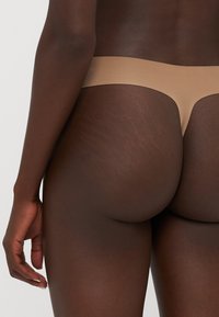 Beige naadloze thong met een zachte textuur, laag uitgesneden ontwerp en minimale bedekking, geschikt voor verschillende huidtinten.