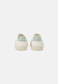 Hvite og mintgrønne sneakers med en glatt lærøvre, teksturert mesh-detaljer og gummisåle. Merkevare synlig på hælen.