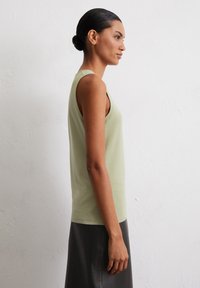 Light green sleeveless top in a soft fabric, featuring a relaxed fit and rounded neckline, worn with a black skirt. Smooth texture, minimalistic design.