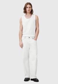 Hvid ribbet tanktop parret med løstsiddende hvide jeans. Modellen bærer sorte sko med en sølvkæde som accent. Enkel, monokromatisk look.