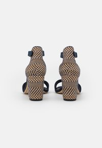Sandali con tacco alto a quadri navy e beige, con cinturini alla caviglia e tessuto testurizzato. Il tacco largo offre stabilità e aggiunge profondità.