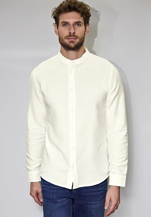 Camisa blanca de manga larga con cuello mao, cierre de botones en el frente y tejido texturizado. Combinada con jeans azul oscuro.