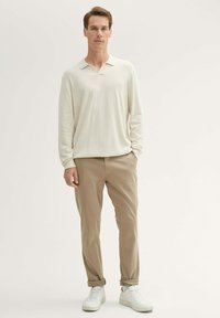 Light beige long-sleeve polo shirt with a v-neck, paired with light brown trousers and white sneakers, featuring a casual fit and simple texture.