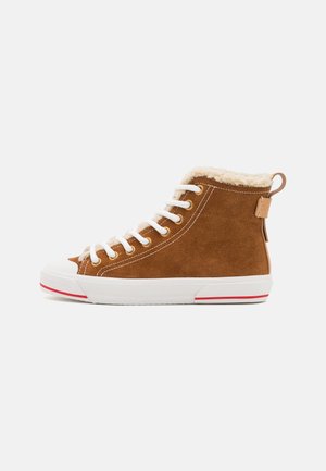 Baskets montantes en daim marron avec des lacets blancs, une semelle en caoutchouc blanche, une bande rouge et une doublure en shearling crème visible au niveau du col.