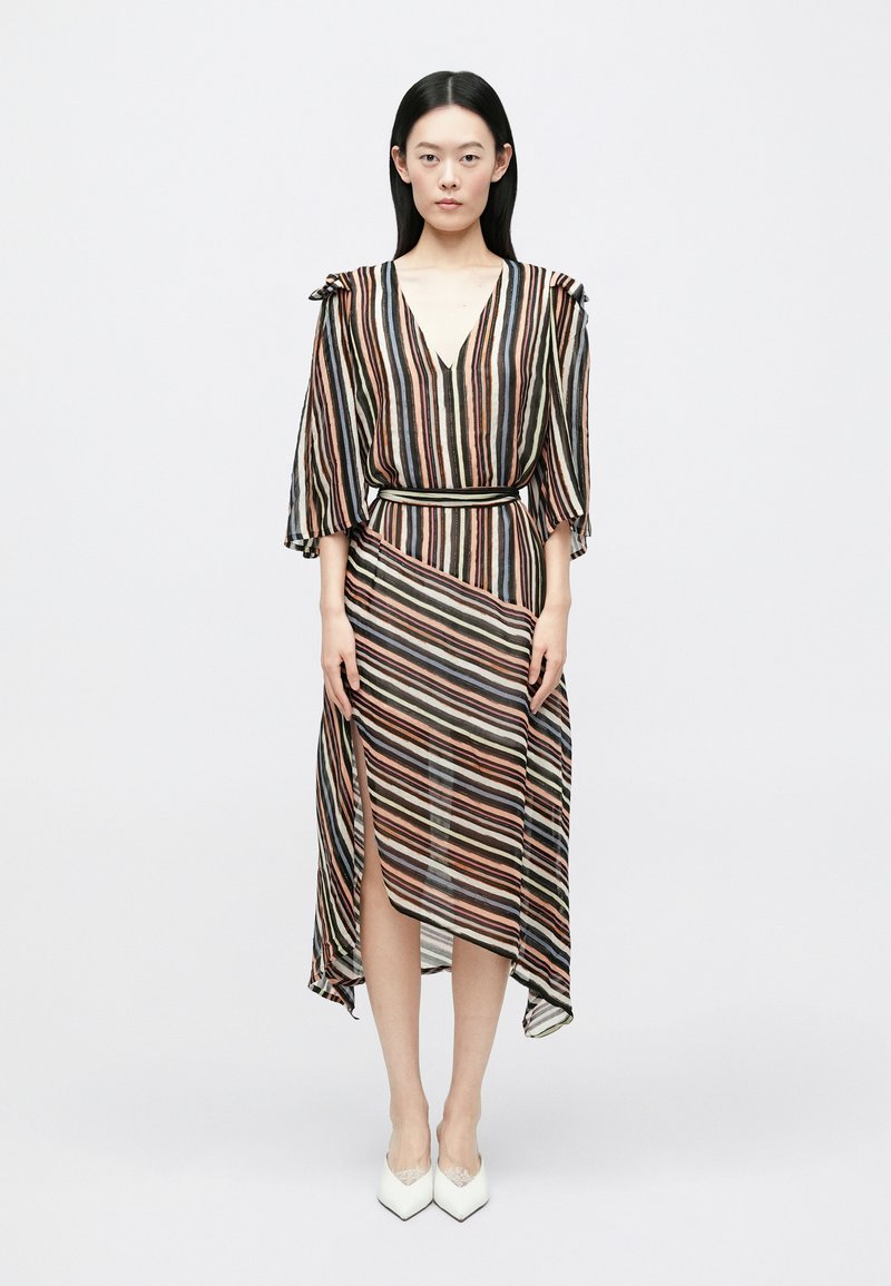 Plūstoša, līdz ceļiem nokarājas kleita ar daudzkrāsainām vertikālām svītrām, V-veida izgriezumu un plūstošām piedurknēm. Ar jostu viduklī un sānu �šķēlumu.