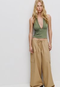 Zelený halter top vyrobený z ribbovaného materiálu, skombinovaný s voľnými béžovými cargo nohavicami s dvoma bočnými vreckami a elastickým pásom na šnúrku.
