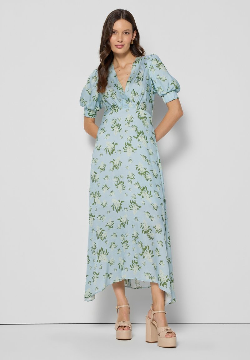 Jasnoniebieska sukienka w kwiaty z bufkami, dekoltem w serek i asymetrycznym dołem. Materiał ozdobiony wzorem zielonych liści. Noszona z beżowymi butami na platformie.