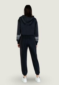 Black cropped hoodie with hood, paired with black joggers featuring elastic cuffs. Sparkling accents on sleeves add detail. White sneakers.