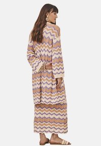 Vestido de punto largo con un patrón en zigzag en tonos púrpura, marrón y crema. Presenta mangas anchas y una silueta relajada, con un tejido texturizado.