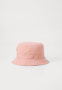 Pink bucket hat made of soft fabric, featuring a wide brim, stitched detailing, and a side tab with a logo. Smooth texture.