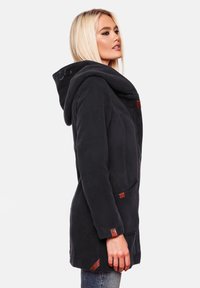 Manteau en polaire noir avec une grande capuche repliée. Présente des boutons-pression et des emplacements en cuir sur les poches. Coupe ajustée, texture douce et longueur mi-cuisse.