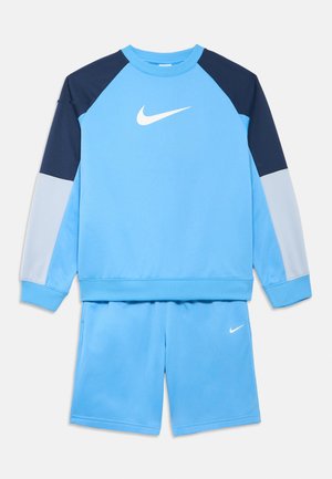 Helehall sinine Nike spordikomplekt, mis sisaldab ümmarguse kaelusega pikka varrukat dressipluusi tumesiniste ja hallide detailidega ning sobivaid lühikesi pükse logoga.