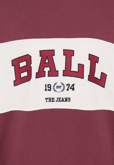 Felpa color bordeaux con una striscia orizzontale bianca su cui è stampato in grassetto "BALL" in lettere rosse, "EST 1974" e "THE JEANS" ricamato in blu navy.