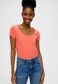 Koraalroze T-shirt met korte mouwen en een ronde halslijn, gedragen met hoge taille blauwe jeans met een knoopsluiting en subtiele vervaging.