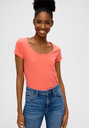 Koraalroze T-shirt met korte mouwen en een ronde halslijn, gedragen met hoge taille blauwe jeans met een knoopsluiting en subtiele vervaging.