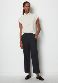 Polo shirt in light beige, short sleeves, with buttoned collar; paired with navy, loose-fitting trousers and black slip-on shoes.