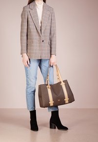 Blazer a scacchi beige e marrone, dolcevita chiaro, jeans blu, stivali neri con tacco; porta una borsa a tracolla marrone a fantasia con manici color crema.